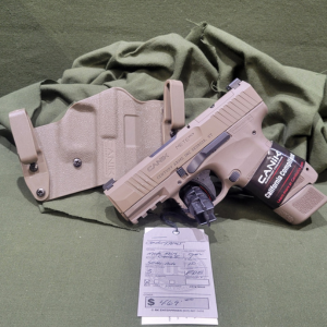 Flat Dark Earth (FDE) semi-automatic pistol with a holster and loaded magazine displayed on a firearm sales counter at Old Town Tactical.