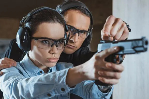 Firearms instructor guiding a student during handgun target shooting practice at an indoor shooting range.