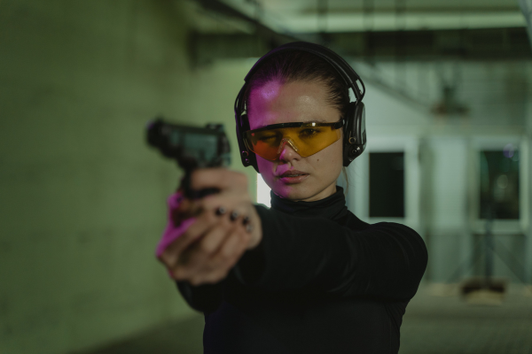 Person aiming a semi-automatic handgun during professional firearms training while wearing protective eye and hearing protection at an indoor shooting range.
